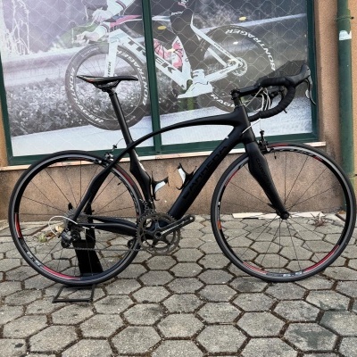 Bicicleta de estrada preta Caltha em suporte num pavimento de lajetas hexagonais