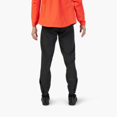 Pessoa de costas a usar calças pretas com texto FOX na perna direita, casaco laranja e sapatos pretos