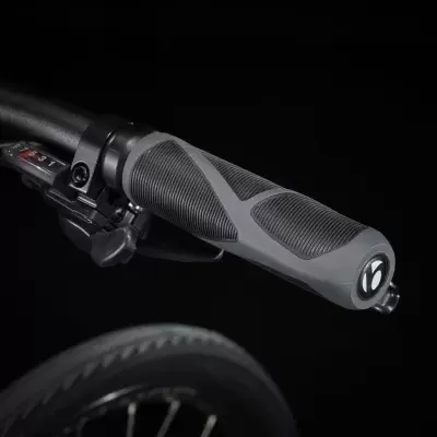 Punho de guiador para bicicleta com borracha preta e cinzenta, botão de controlo e pneu ao fundo.