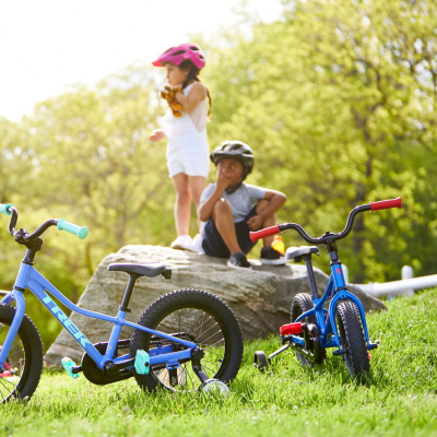 Duas bicicletas infantis azuis com punhos coloridos em relva e duas crianças ao fundo