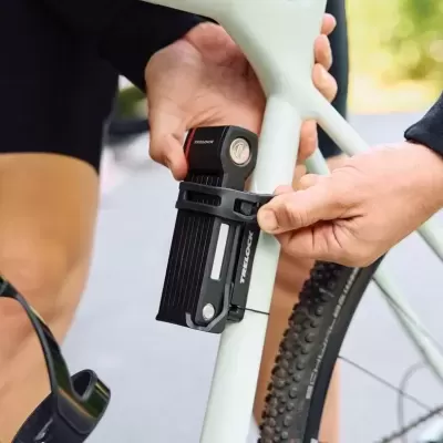 Fechadura dobrável preta TRELOCK fixada no quadro branco de uma bicicleta com pneus de cravos