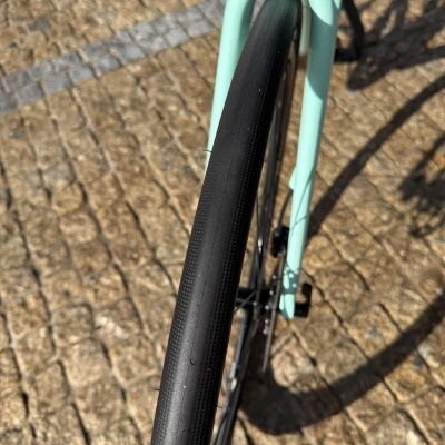 Roda dianteira de bicicleta com pneu preto e garfo verde água sobre pavimento de pedra