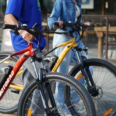 Duas bicicletas de montanha vermelha e amarela seguradas por pessoas junto a um café