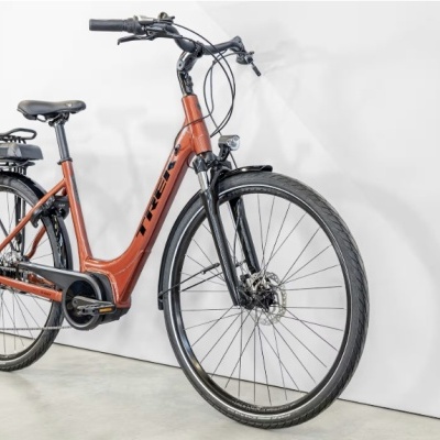 Bicicleta elétrica laranja com pneus pretos e assento preto junto a parede branca