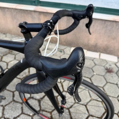 Guiador de bicicleta de estrada preto com travões e cabos brancos junto a parede e janela