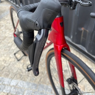 Punho de bicicleta Shimano preto com quadro vermelho e pneu castanho sobre pavimento urbano
