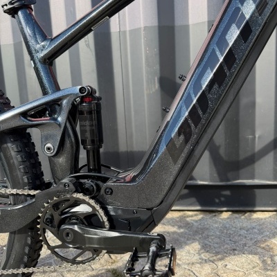 Quadro de bicicleta preta metálica com suspensão traseira e pedal de plataforma num chão de pavê.