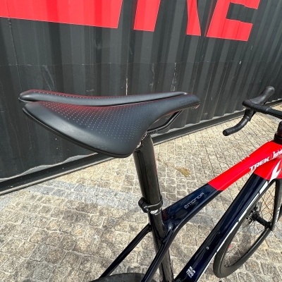Bicicleta de estrada Trek preto e vermelho com selim preto perfurado ao lado de contentor preto com letras vermelhas