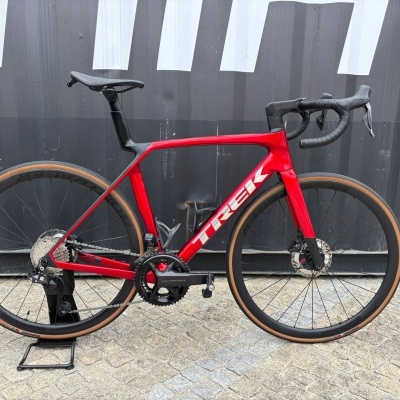 Bicicleta de estrada vermelha e preta com pneus castanho claro e quadro com o texto TREK.