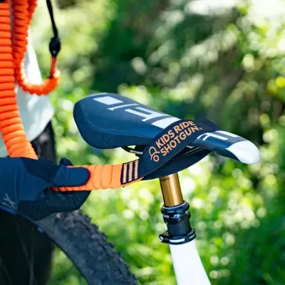 Sela de bicicleta infantil preta com texto laranja e detalhes brancos junto a corda elástica laranja