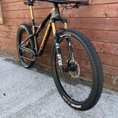 Bicicleta de montanha Orbea preta e dourada encostada numa parede de madeira