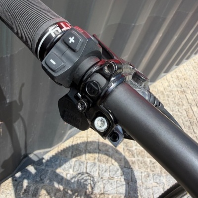 Punho e comandos eletrónicos em guiador de bicicleta preto com detalhes em vermelho e branco.
