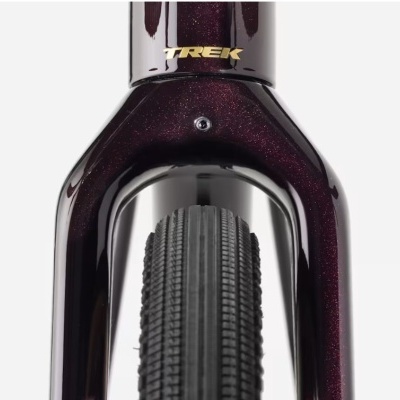 Bicicleta roxo escuro próximo da roda da frente com texto TREK em dourado.