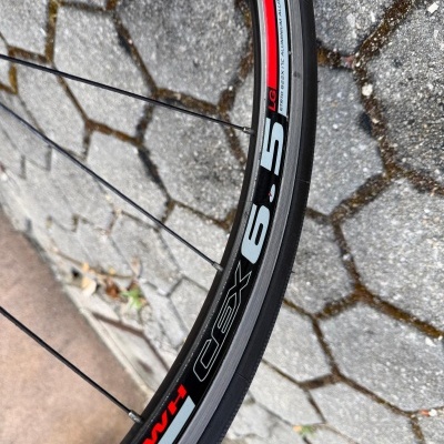 Roda de bicicleta com aro preto, vermelho e cinza e texto WT cex 65 LG em calçada de pedra.