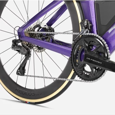 Roda traseira e sistema de transmissão de bicicleta roxa metalizada com pneus pretos e detalhes em bege.