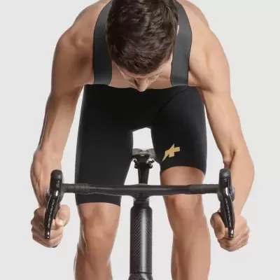 Homem a usar calções de ciclismo pretos com alças largas e símbolo amarelo, em bicicleta de estrada preta com guiador preto.