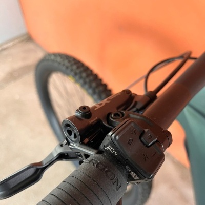 Punho preto de bicicleta com controle eletrónico e manete de travão, fundo laranja.