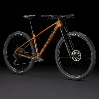 Bicicleta de montanha cor cobre com pneus Maxxis e suspensão dianteira sobre fundo negro