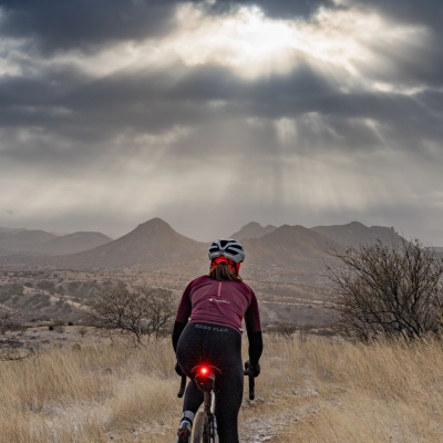Pessoa a andar de bicicleta em caminho de terra com céu nublado e raios de sol