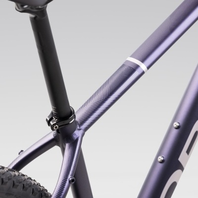 Estrutura de bicicleta roxa metálica com padrão texturizado e parafuso de aperto, pneu preto visível.