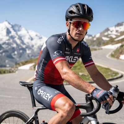 Ciclista com fato OAKLEY em bicicleta de estrada com montanhas nevadas ao fundo