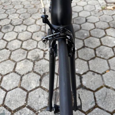 Travão dianteiro preto de bicicleta com aro de carbono numa superfície de blocos hexagonais.