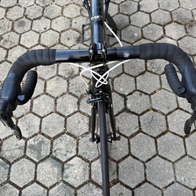 Guiador de bicicleta de estrada preto com punhos envoltos em fita preta e cabos brancos