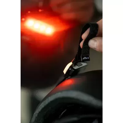 Mão a segurar correia preta de velcro num capacete preto com luz vermelha ao fundo