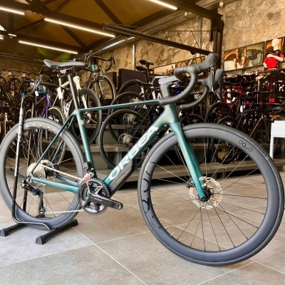 Bicicleta de estrada Orbea verde-azulada com rodas pretas numa loja de bicicletas