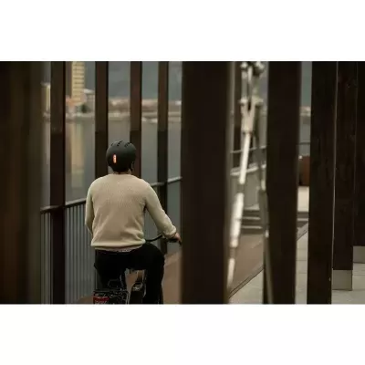 Homem de costas com camisola bege e capacete a andar de bicicleta num passadiço de madeira