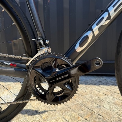Bicicleta de estrada preta com pedaleira Shimano 105 e fundo de pavimento de pedra
