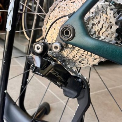 Peça de bicicleta metálica com corrente e desviador Shimano 105 em fundo de piso de azulejo cinza