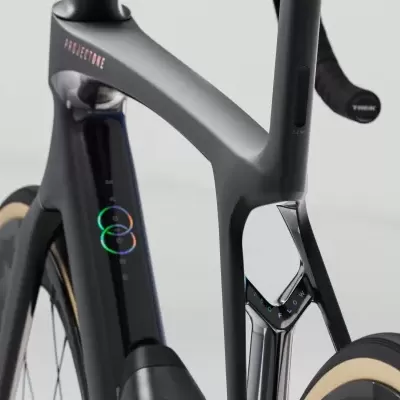 Detalhe da estrutura de uma bicicleta de estrada preta com texto PROJECT ONE e círculos coloridos no tubo vertical.