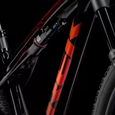 Detalhe do quadro preto e vermelho de uma bicicleta com letras GT laranjas e pneus pretos