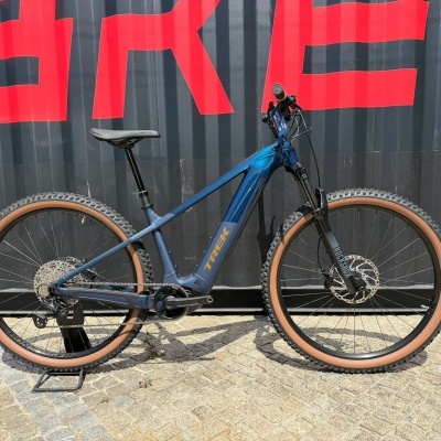 Bicicleta de montanha azul com pneus castanhos num chão de pedras com fundo preto e vermelho.