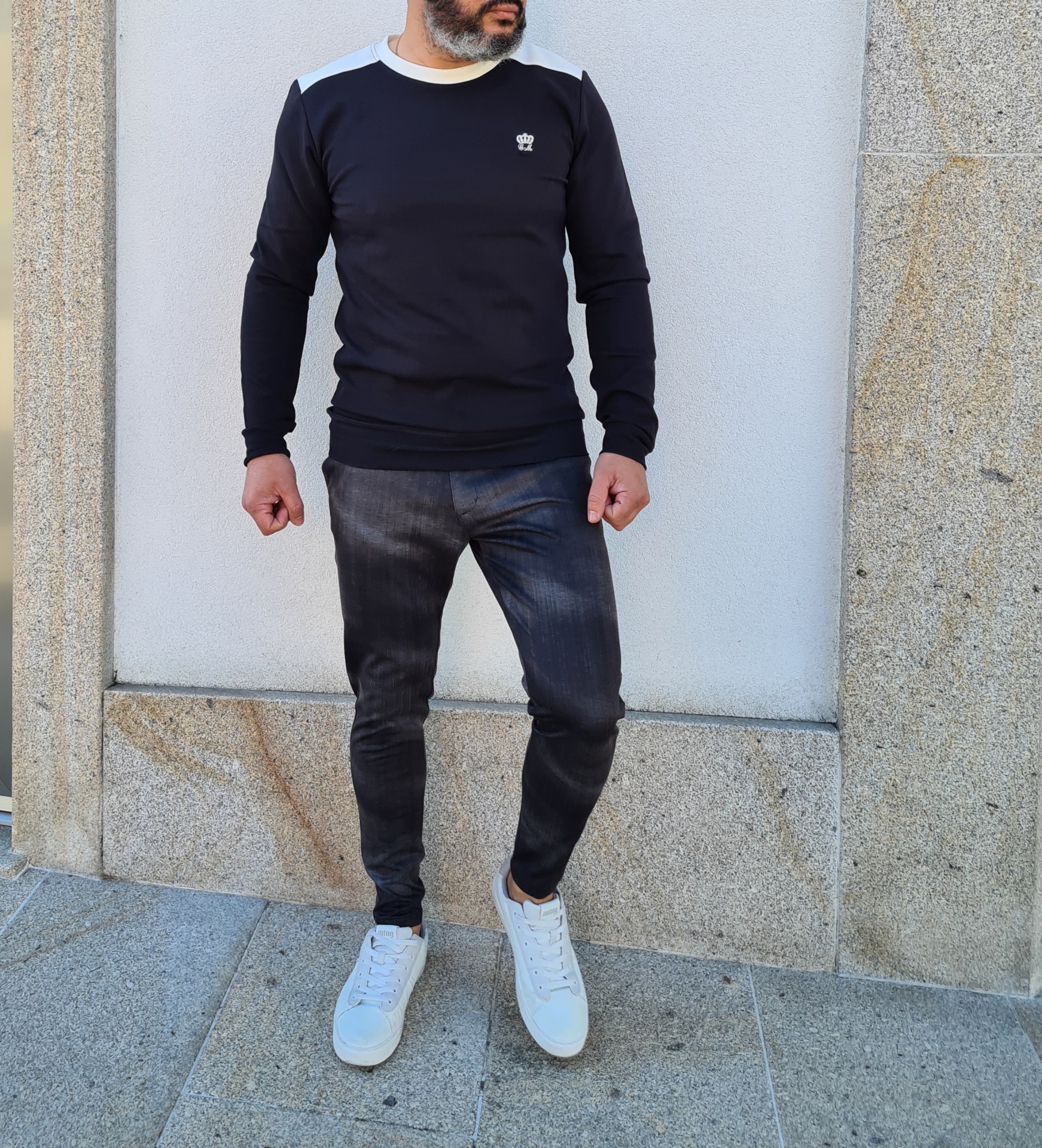 CALÇAS TECIDO SLIM FIT Homem com sweatshirt preta, jeans escuros e ténis brancos em piso de pedra