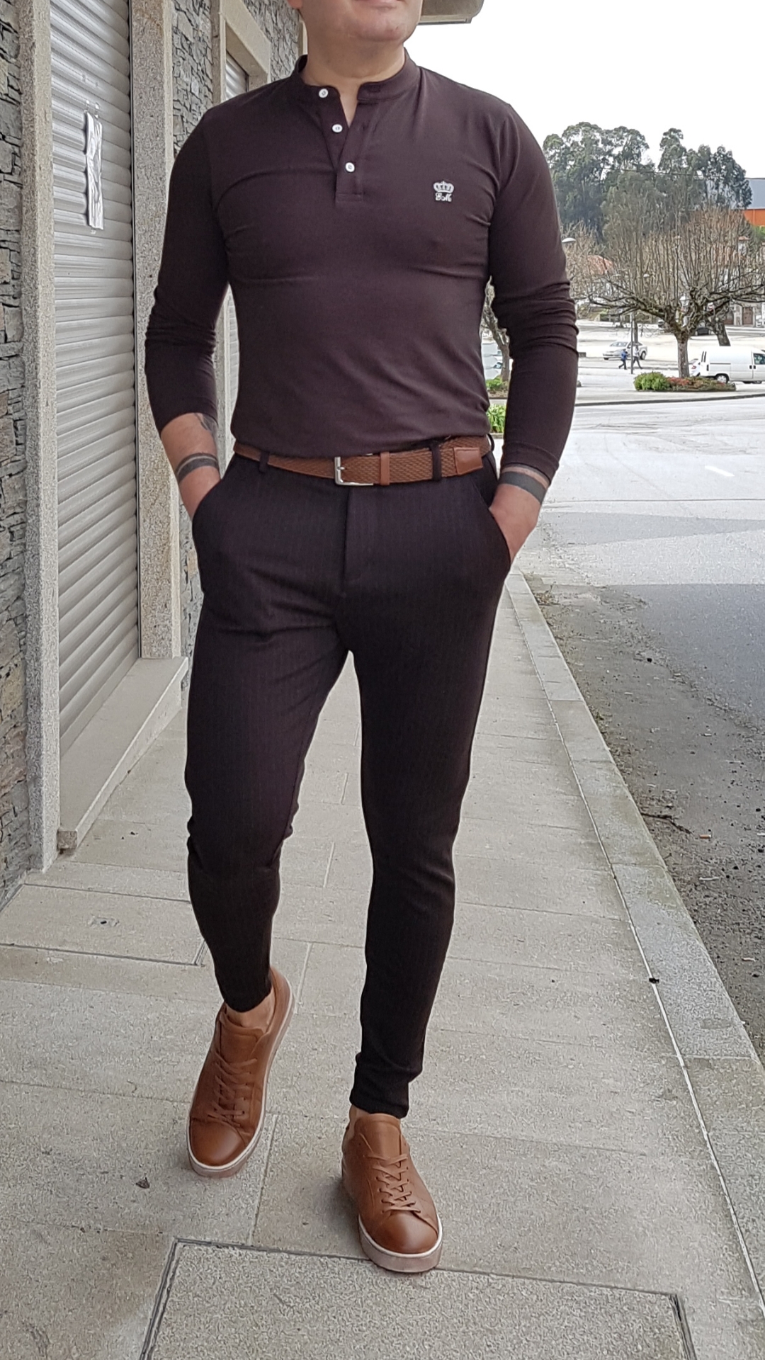 CALÇAS TECIDO SLIM FIT,CASTANHO ESCURO Homem com camisa preta de manga comprida, calças e cinto castanho, e sapatos castanhos