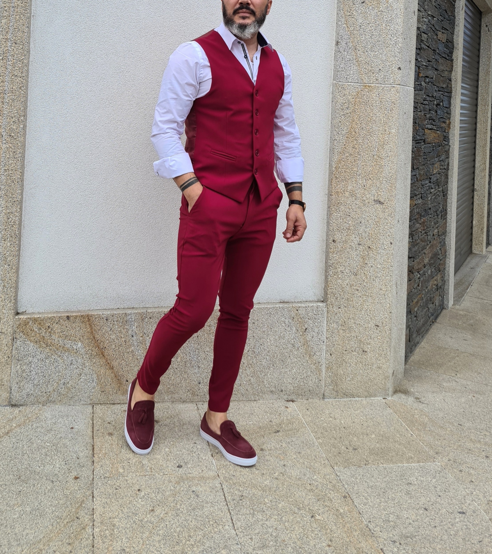 Calça cor cereja Homem com colete e calças vermelhas, camisa branca e sapatos castanho-escuros num piso de pedra junto a muro