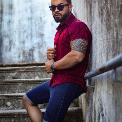 Homem com camisa vermelha e calções de ganga azuis sentado em escadaria