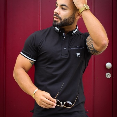 Homem com camisa polo preta e calças claras contra porta vermelha