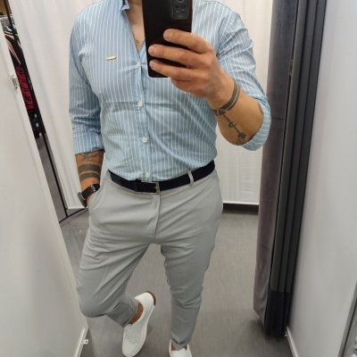 Homem com camisa azul riscada e calças cinza em selfie de espelho