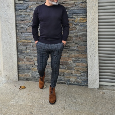 Homem vestido com camisola preta, calças cinzentas xadrez e botas castanhas em ambiente exterior
