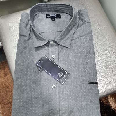 Camisa cinzenta de manga comprida com padrão de pequenas bolinhas brancas dobrada sobre superfície prateada