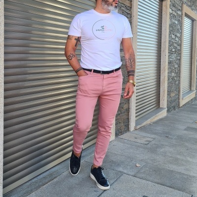 Homem com t-shirt branca, calças rosa claro e ténis pretos numa calçada urbana
