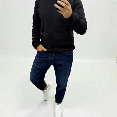 Homem com camisola preta, jeans azuis e ténis brancos a tirar selfie