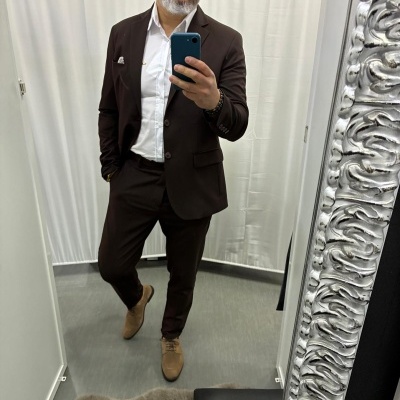 Homem com fato castanho, camisa branca e sapatos castanhos em frente a espelho