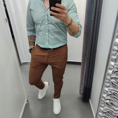 Homem de camisa verde às riscas brancas e calças castanhas a tirar selfie em provador