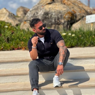 Homem sentado em escadas ao ar livre com roupa casual e tatuagens