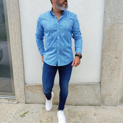 Homem com camisa azul clara, calças de ganga azul escuro e sapatilhas brancas em passeio de pedra