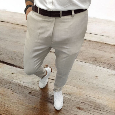 Calças sociais bege, cinto castanho escuro e sapatilhas brancas em chão de madeira clara